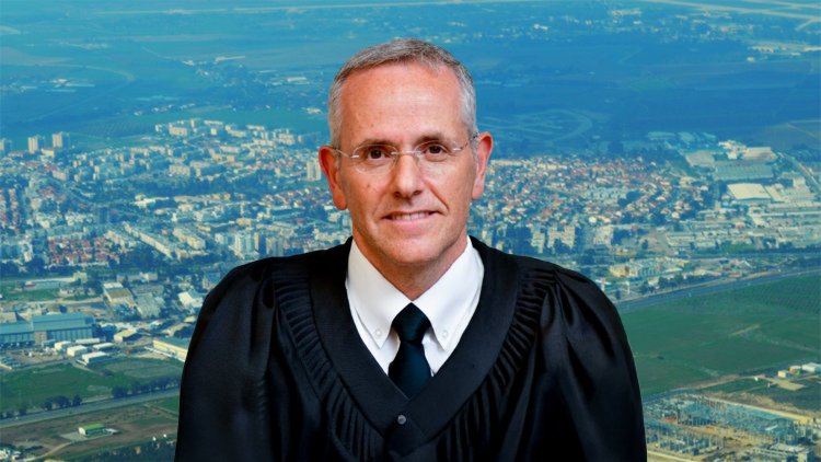 השופט דוד מינץ על רקע קריית מלאכי (אתר הרשות השופטת, עמוס מרון, ויקימדיה)